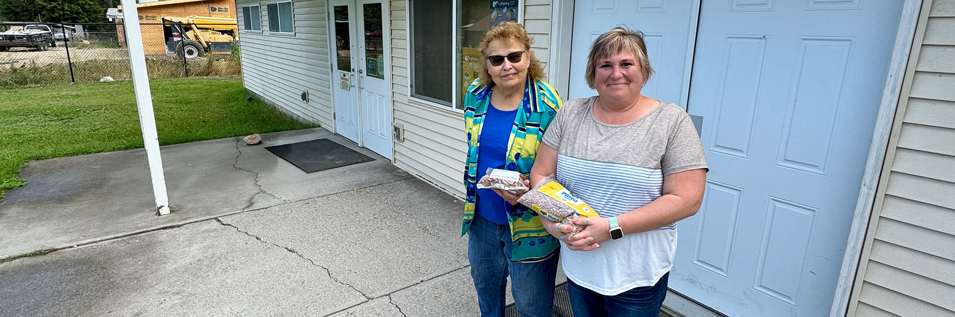 Two women stand outside Springdale Food Pantry, they both are holding a bag of dried beans.