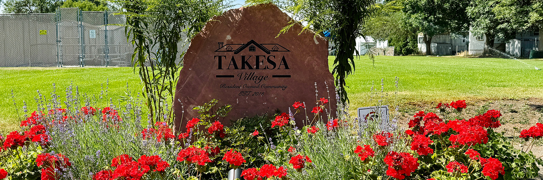 Red flowers in front of a stone sign that says Takesa Village outside.