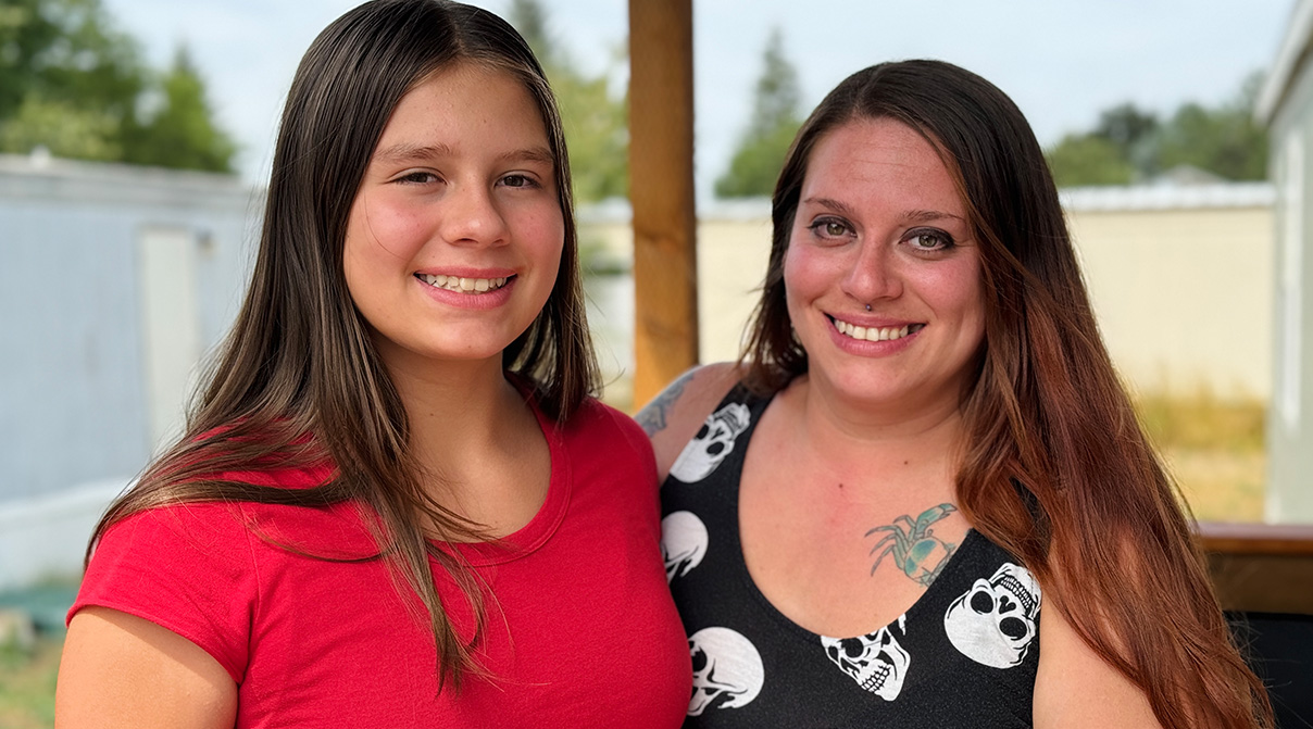 Mother and daughter stand outside in the backyard of their new home, smiling.