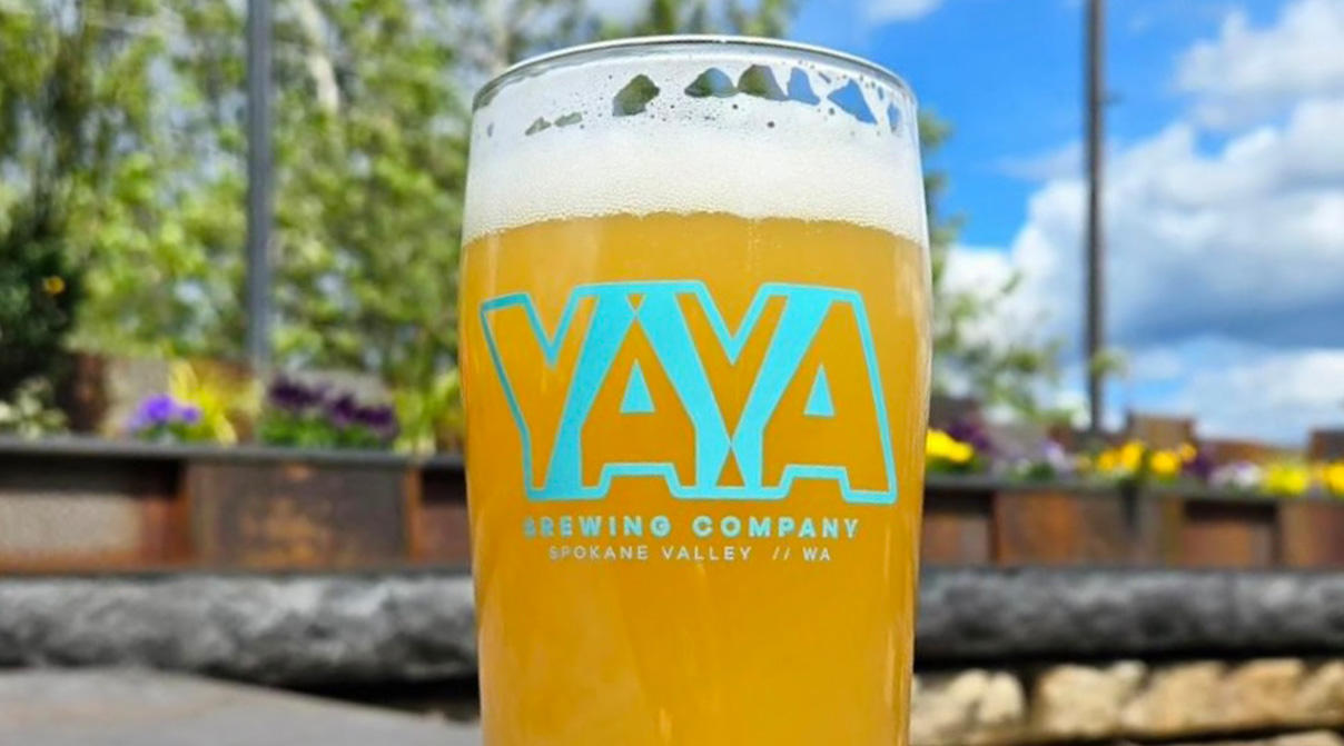 Tall glass with freshly poured beer inside, the glass has teal lettering on it that says YAYA Brewing Company Spokane Valley, WA.