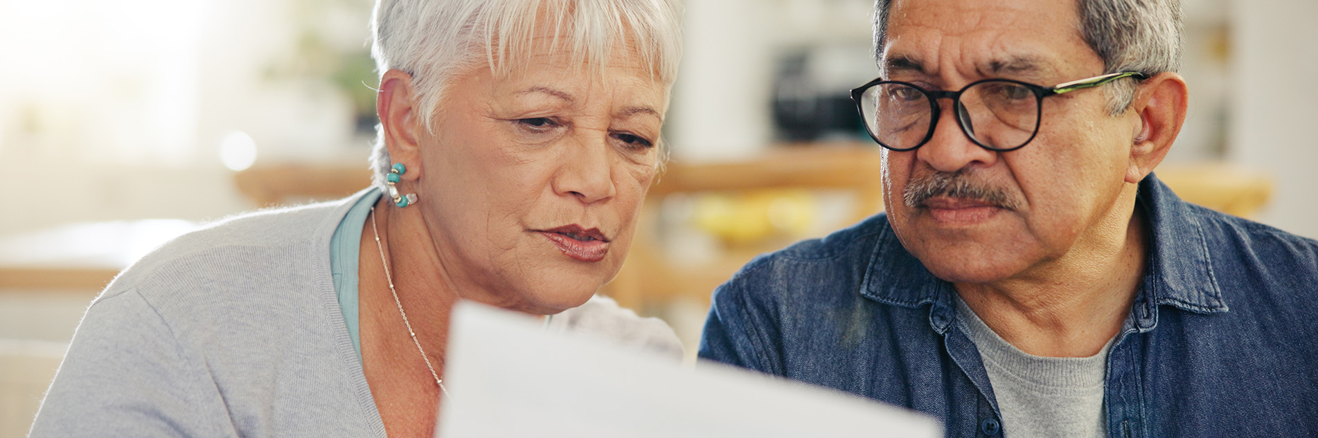 Older man frowns as he looks at a piece of a paper an older woman is holding up towards him.
