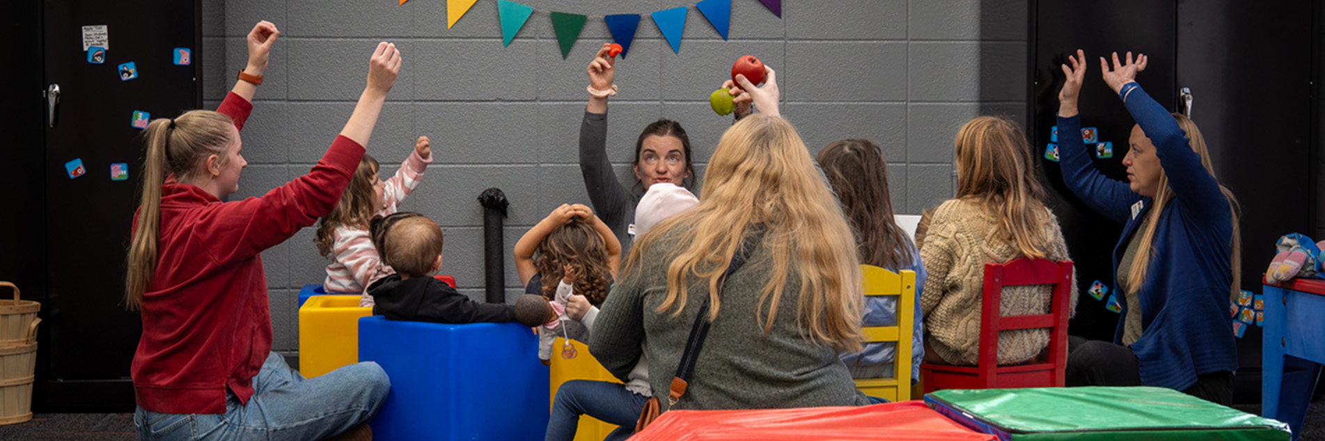 Group of children and parents raising their hands in a game at school.