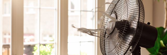 Electric fan with blowing ribbons in front of window on hot summer day.