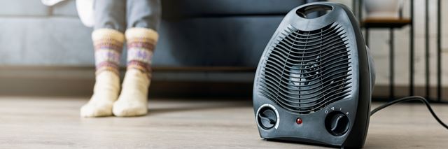 Electric space heater sitting on the ground in front of a person who is sitting on a couch, the person is wearing thick winter socks.