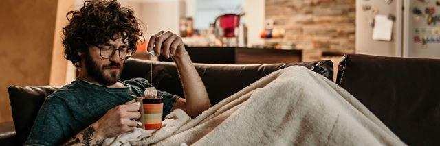 Man lounging on couch with a blanket and a mug of tea.