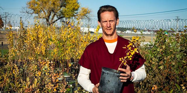 Male inmate smiling holding small potted tree