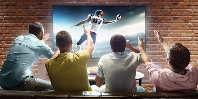 Four men sitting on a couch watching football on the tv and cheering