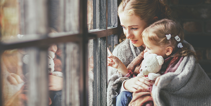 Mother and daughter, wrapped in blanket, sitting by window