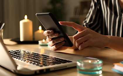 Close up of hands using smart phone during power outage with candles at night on a desk at home.