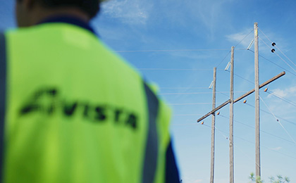 Person wearing a yellow vest with Avista written on the back stands in the foreground with power poles in the background.