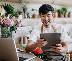 Owner of a flower shop uses a digital tablet against flowers and plants