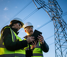 A man and woman work on a tablet outside under a powerline.