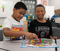Two children are playing a board game and smiling.