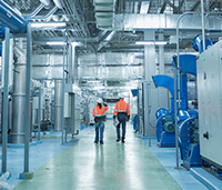 Two people in orange safety vests inspect industrial building.
