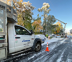 Avista truck on a snowy street with linepeople working on a pole in the background