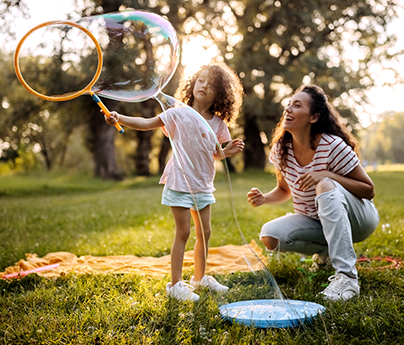 Mother and daughter are outside blowing bubbles on a sunny day.