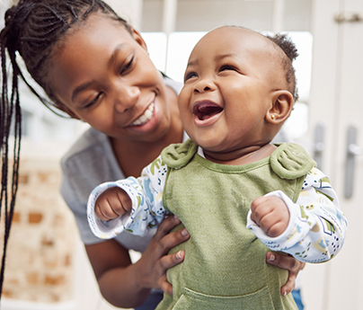 A smiling mother holds a smiling toddler in her arms.