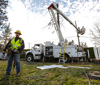 Linemen working near a bucket truck with broken branches on the ground after a storm