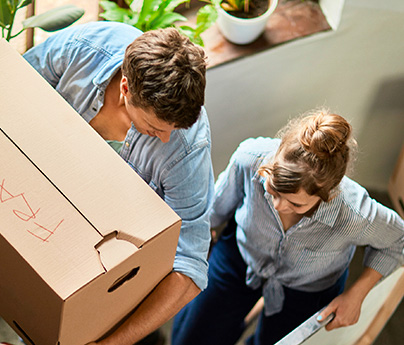 Man carries moving box upstairs while woman follows him