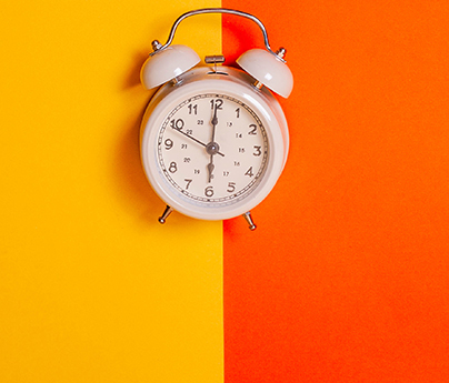 White vintage alarm clock on two tone solid color yellow and orange background.