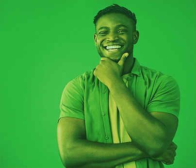 Smiling man has his hand on his chin like he is thinking, standing in front of a green background.