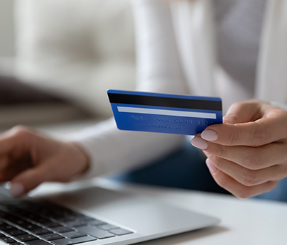 Woman holds credit card in one hand while typing on her laptop with the other hand.