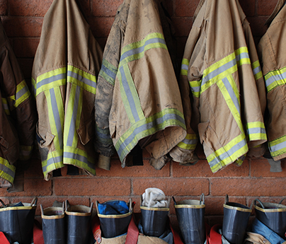 Firefighter jackets hanging up with firefighter boots lined up below against the wall.