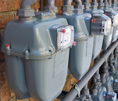 Natural gas meters in a row outside against the wall.