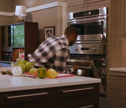 Man opens oven to smell inside of it, there are vegetables on the kitchen counter as he was in the middle of preparing a meal.